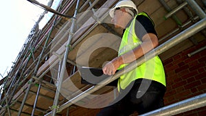 Male builder foreman construction worker on building site wearing a hardhat writing on clipboard