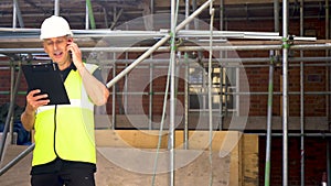 Male builder foreman construction worker on building site wearing a hardhat writing on clipboard