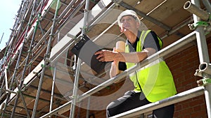 Male builder foreman worker on construction building site standing on scaffolding writing on clipboard