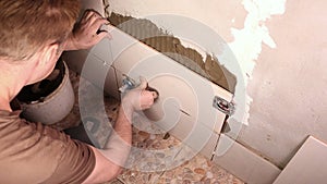 male builder glues light tiles to the wall in the bathroom