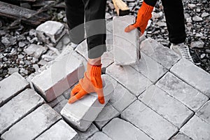 A male builder in a hard hat and protective gloves unloads bricks at a construction site