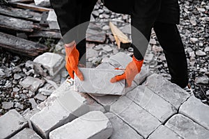 A male builder in a hard hat and protective gloves unloads bricks at a construction site