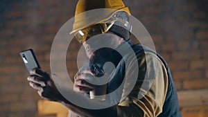 Male builder with hot drink using smartphone