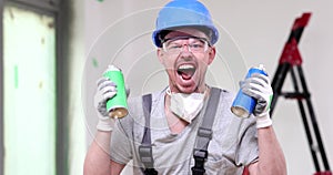 Male builder shaking paint sprayers screams in light room
