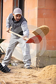 male builder shuvelling sand on building development