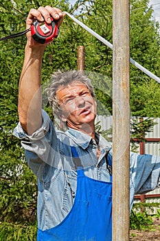 Male Builder with a tape measure on a real construction site in nature. Measures the distance between the posts with a