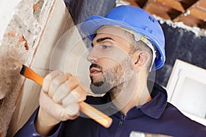 Male builder using hammer chisel on interior wall