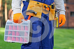 Male builder wearing tool belt carrying toolbox at construction site. Close up on waist area