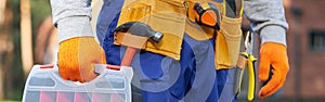 Male builder wearing tool belt carrying toolbox at construction site. Close up on waist area