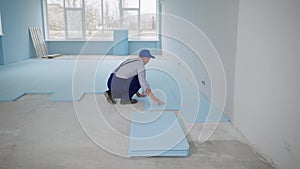 male builder in work uniform insulates floor with polystyrene foam to lay laminate indoors