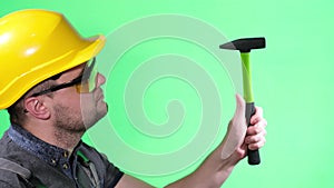 Male builder in yellow helmet and goggles working with hammer, on green background chromakey,