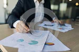 Male business analyst writing on papers, checking data, charts and graphs, sitting at desk in office, closeup, cropped