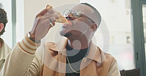 Male business employe eating pizza with colleagues during a relaxed lunch break indoors, showcasing togetherness and