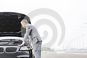 Male business executive looking at breakdown car against sky