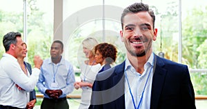 Male business executive smiling at camera while colleagues discussing over laptop