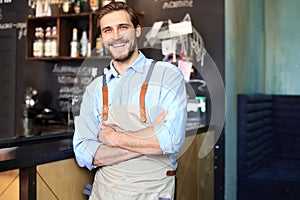 Male business owner behind the counter of a coffee shop with crossed arms, looking at camera