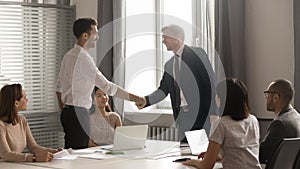 Male business partners negotiators handshake at group office meeting negotiations