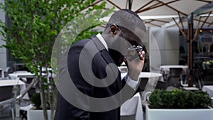 Male in business suit passing by luxury open air cafe talking over cell phone