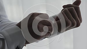 Male businessman fastens cufflinks on sleeves by the window.