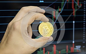 Male businessman hand holding bitcoin on a background of growth graph on a screen of laptop. Virtual money concept and