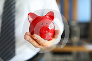 Male businessman hold in hand red little piggybank