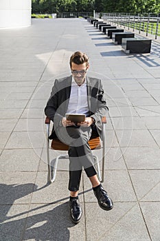 Male businessman or worker in black suit with tablet sitting on chair