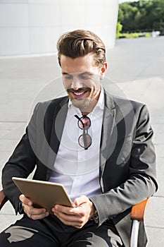 Male businessman or worker in black suit with tablet sitting on chair