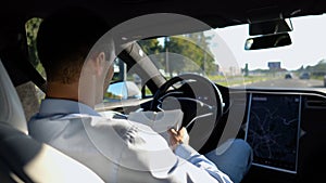 Male businessperson reading book during riding on electrical vehicle with autopilot at urban road. Successful