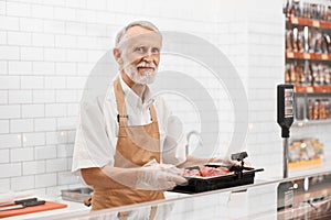 Male butcher demonstrating meat in supermarket.