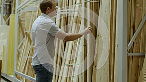 Male buyer chooses wooden boards in shop of building materials