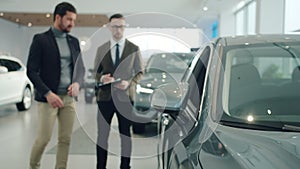 Male buyer choosing brand new car in showroom discussing deal with manager. Focus on vehicle mirror