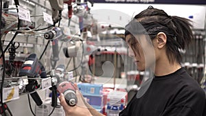 A male buyer looks at a tool in a hardware store. Asian man in a building supermarket