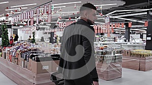 Male buyer with plastic basket walks through grocery store looks around in search of goods. Caucasian customer 30 35