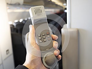 Male cabin crew holding interphone in aircraft cabin.