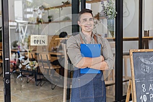 A male cafe employee standing in front of the store greets customers and has a sign that says open to show that the shop is open.