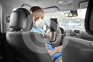 Male car driver in mask showing smartphone