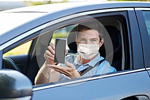 Male car driver with smartphone wearing face mask
