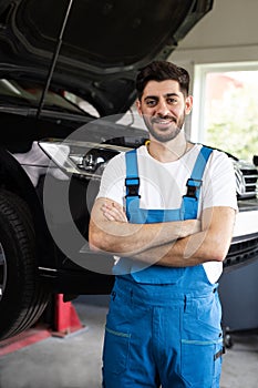 Male car mechanic at workplace in spacious repair shop. Portrait of bearded car mechanic crosses hands in a car workshop