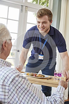 Male care worker serving dinner to a senior man at his home