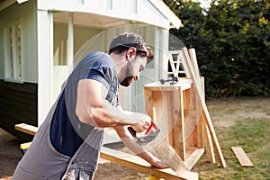 Male Carpenter With Female Apprentice Sawing Wood To Build Outdoor Summerhouse In Garden photo