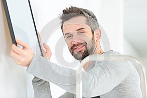 Male carpenter hanging picture frame on wall at home