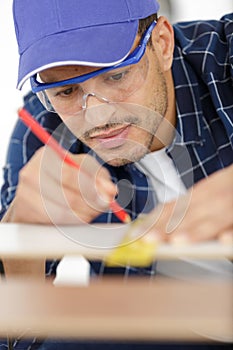 male carpenter measuring wood using pencil