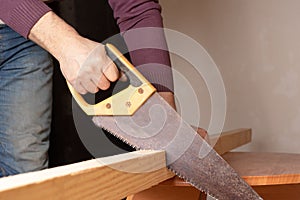 A male carpenter saws a wooden board with a hand saw. Repair of a house or apartment, construction and creation of furniture