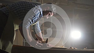 Male carpenter in shirt in dark workshop planing wood