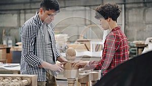 Male carpenter talking to female apprentice in workshop discussing woodware