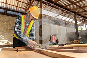 A male carpenter using pencil on a piece of wood on construction site