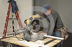 Male carpenter wearing tool belt and cutting wood board with professional chop saw on construction site home remodel