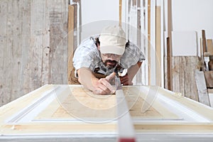 Male carpenter working the wood in carpentry workshop, checking level of wooden door with bubble level, wearing overall