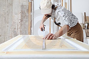 Male carpenter working the wood in carpentry workshop, measuring wooden door with a mesure tape, wearing overall and cap
