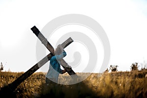 Male carrying a handmade wooden cross on his back in a grassy field